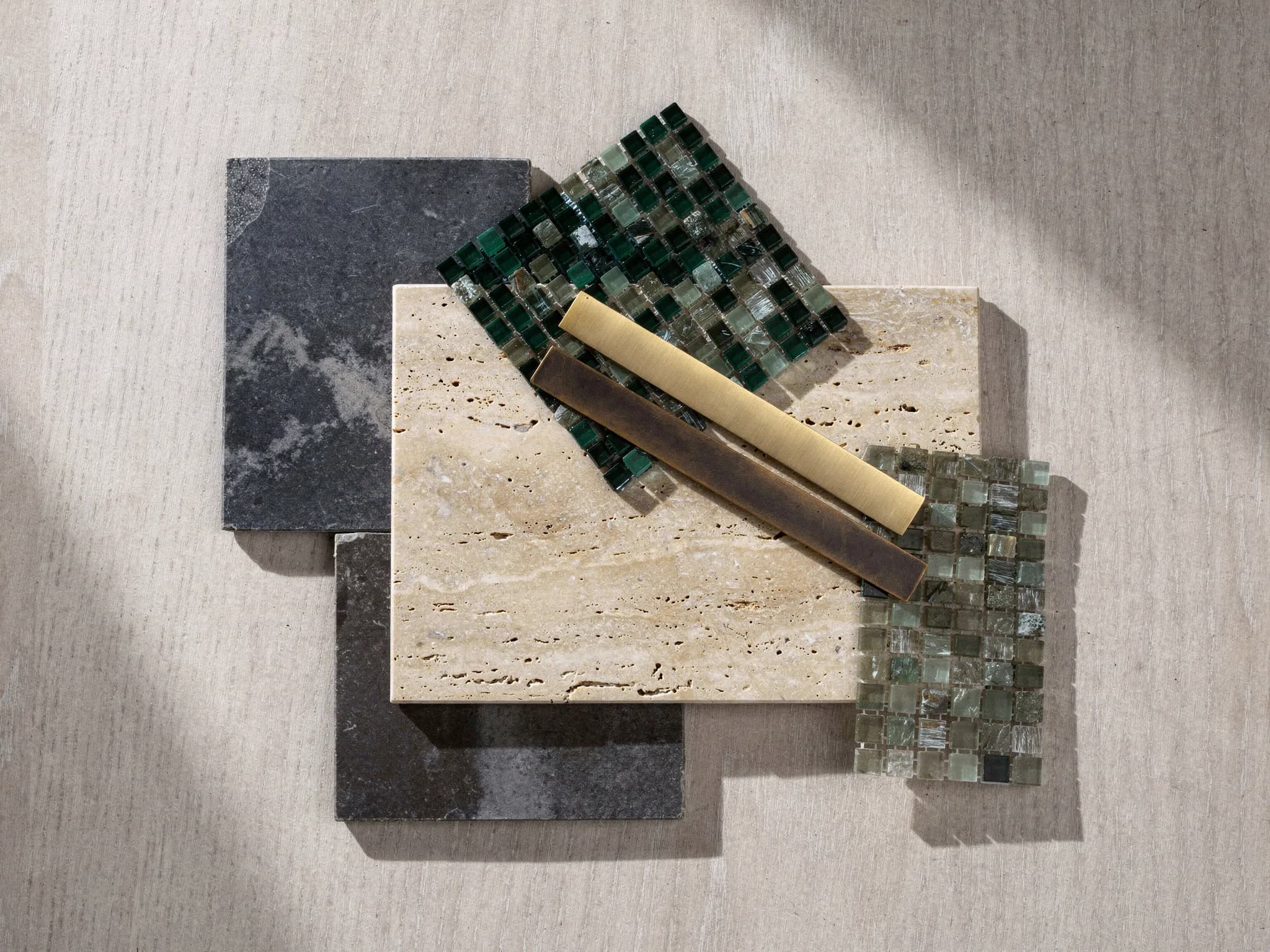 Materiaalpalet met stalen van blauwsteen, kalksteen en travertijn, mozaïekvellen in groentinten en stalen in geborsteld messing en brons
